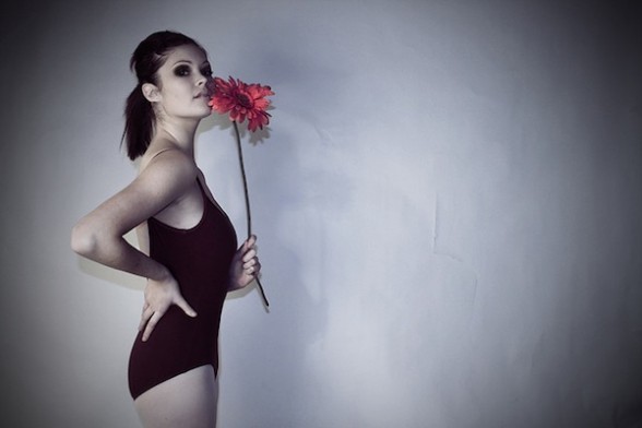 A dancer in leotard and tights holds a single red flower.