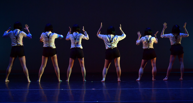 Six dancers in white shirts with black suspenders face upstage.