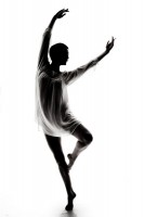 A dancer, her face and form eclipsed by shadow, arcs her body