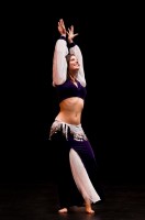 IMAGE A belly dancer poses with arms above her head, a confident smile on her face. IMAGE