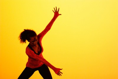 A dancer in red spreads arms on a yellow stage