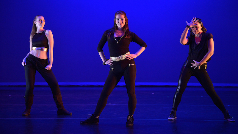 Three dancers in black against a blue backdrop
